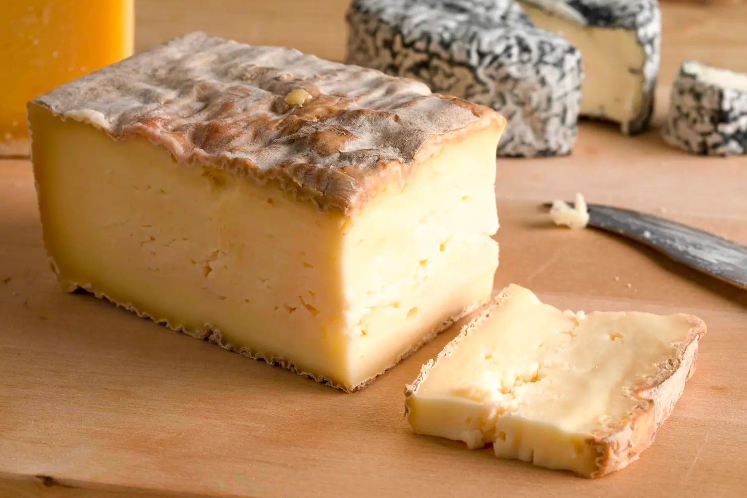 un pezzo di taleggio appena tagliato su un tagliere di legno con un coltello vicino